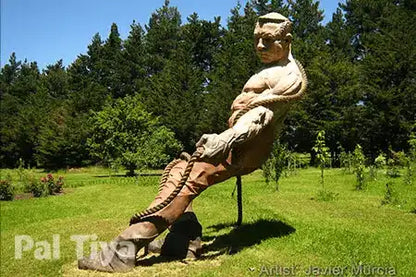 A large outdoor sculpture, made from Pal Tiya Premium, of a muscular male figure pulling hard on a huge rope, placed on a grassy lawn with trees and blue sky behind it.  'Artist: Javier Móroa' appears at lower right.