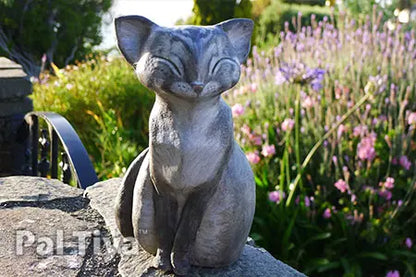 A gray cat garden statue with closed eyes sits on a stone ledge in a sunlit garden with green foliage and pink flowers in the background. Made with Pal Tiya Premium